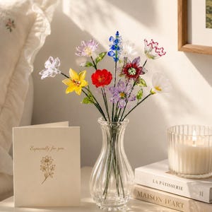 May include: A clear glass vase containing a bouquet of multi-colored glass flowers in shades of red, yellow, blue, purple, and white, each with green glass stems and leaves, accompanied by a folded greeting card with the text Especially for you.