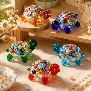 May include: Five glass turtle figurines with colorful millefiori patterned shells. Each turtle has a solid-colored head and legs in amber, blue, green, light blue, or red. The small decorative sculptures feature intricate floral glass designs.