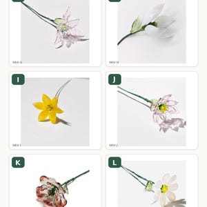 May include: A collection of six glass flower stems labeled G through L. Each stem features a unique glass bloom in colors including pink, white, yellow, and red, attached to a thin green wire stem with small green glass leaves for display.