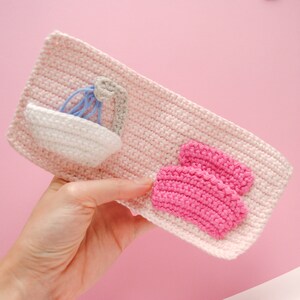 May include: A pink crocheted pouch with a white crocheted sink and a pink crocheted bath mat.