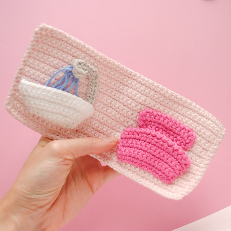 May include: A pink crocheted pouch with a white crocheted sink and a pink crocheted bath mat.