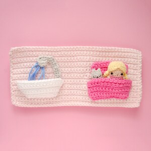 May include: A pink crocheted wall hanging with a white bathtub and a pink bed with a doll and a cat inside.