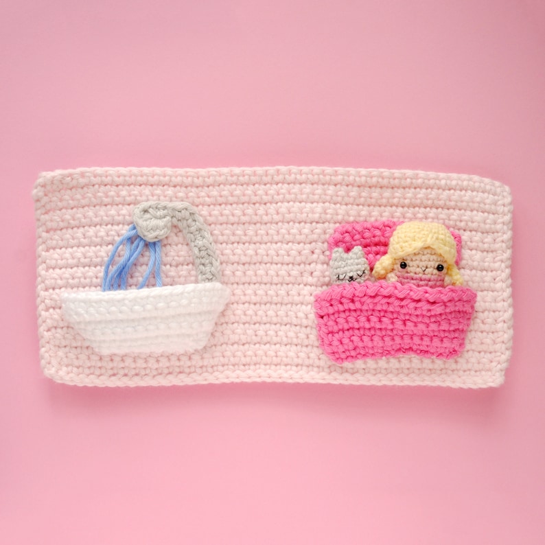 May include: A pink crocheted wall hanging with a white bathtub and a pink bed with a doll and a cat inside.