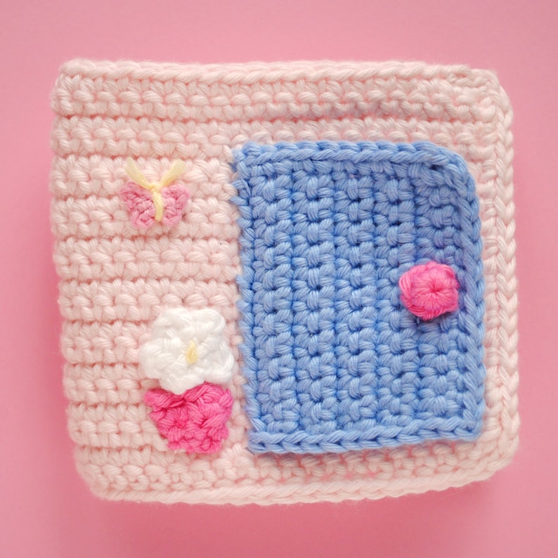 May include: A pink crocheted square with a blue crocheted square inside. The blue square has a pink flower in the corner. The pink square has a white flower and a butterfly.