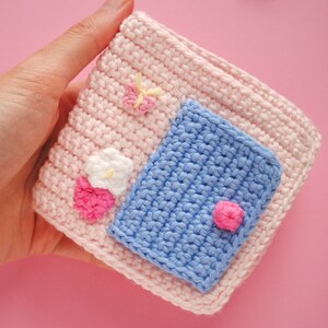 May include: A pink crocheted pouch with a blue crocheted pocket and pink and white flower embellishments.