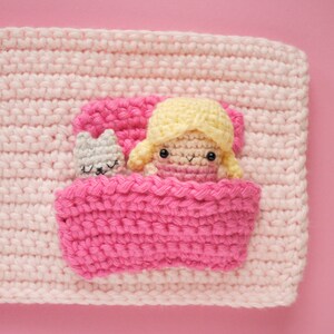 May include: A crocheted pink blanket with a pink bed and a doll with yellow hair and a grey cat inside.