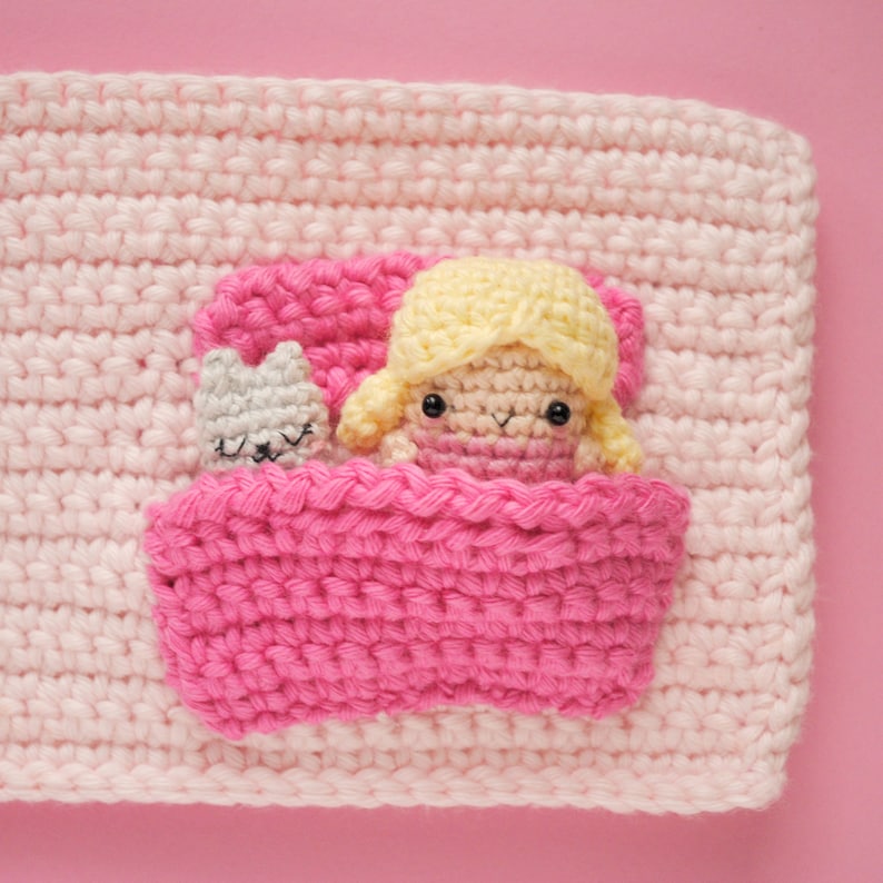 May include: A crocheted pink blanket with a pink bed and a doll with yellow hair and a grey cat inside.