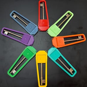 May include: Eight metal skeleton keys are each encased in a colourful, elongated, trapezoidal plastic holder. The holders are arranged in a circular pattern and come in red, light green, orange, teal, yellow, bright green, purple, and blue.