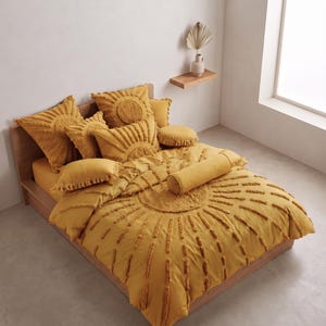 May include: A mustard yellow bedding set featuring a tufted sunburst pattern on the duvet cover and matching square, rectangular, and round throw pillows. The set includes a long cylindrical bolster pillow, all in a solid, textured fabric.