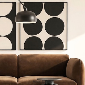 May include: A brown velvet sofa positioned below two square wall art pieces featuring a black and white polka dot pattern. A black dome-shaped pendant light hangs above the sofa, and a small black circular side table sits in the foreground.