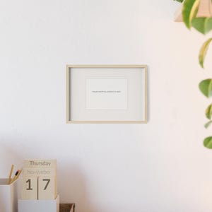 Peut inclure: Un cadre en bois clair contenant une impression rectangulaire blanche avec le texte allemand "Heute reicht es, präsent zu sein." Le cadre est fixé sur un mur blanc uni, positionné au-dessus d'un petit calendrier en bois indiquant jeudi 17 novembre.