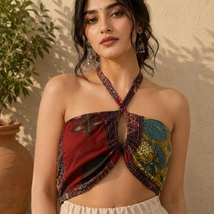 May include: A halter-style crop top featuring a patchwork design with contrasting panels in deep red, mustard yellow, and teal. The fabric displays intricate floral and botanical patterns with visible stitching details, a central cutout, and thin straps.