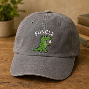 May include: A charcoal gray baseball cap featuring an embroidered graphic of a green crocodile wearing black sunglasses and holding a white ice cream cone. Above the crocodile, the word FUNCLE is embroidered in white capital letters.