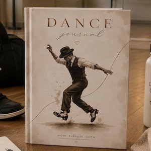 May include: A hardcover dance journal with a beige cover featuring a sepia-toned illustration of a dancer in a hat and vest. The text reads DANCE journal and MOVE. EXPRESS. GROW. The journal is surrounded by a black dance bag, sneakers, a water bottle, and a spiral notebook.