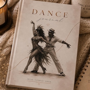 May include: A hardcover dance journal with a beige cover featuring a sepia-toned illustration of a dancing couple. The text reads DANCE journal and MOVE. EXPRESS. GROW. with small heart icons. The journal is surrounded by a candle, a mug, and a notebook.
