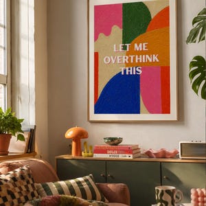 Op de afbeelding: Een ingelijste rechthoekige wandprint met abstracte vormen in levendige kleuren, waaronder roze, groen, oranje, rood en blauw. De tekst "LET ME OVERTHINK THIS" staat in witte hoofdletters in het midden van het kunstwerk gedrukt.