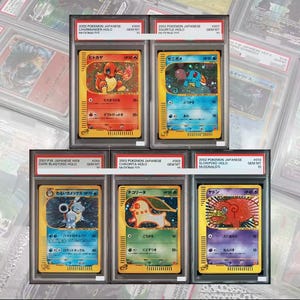 Puede incluir: Cinco cartas coleccionables Pokemon graduadas en fundas protectoras de plástico. La fila superior muestra un Charmander y un Squirtle japoneses de 2002. La fila inferior contiene un Dark Blastoise Web, un Chikorita y un Slowpoke japoneses.