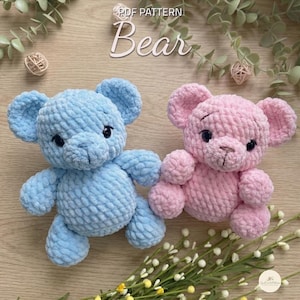 May include: Two crocheted plush bears, one light blue and one light pink, featuring round ears, dark plastic eyes, and stitched noses. The text "PDF PATTERN Bear" is visible at the top. The bears have a textured, soft yarn appearance.