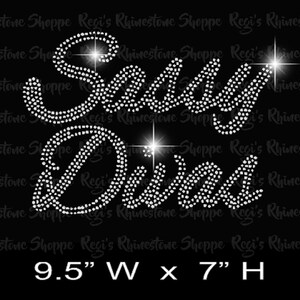 Pode incluir: Um design de strass que lê "Sassy Diva" em uma fonte cursiva. O design tem 9,5 polegadas de largura e 7 polegadas de altura. O design é feito de 977 strass transparentes.