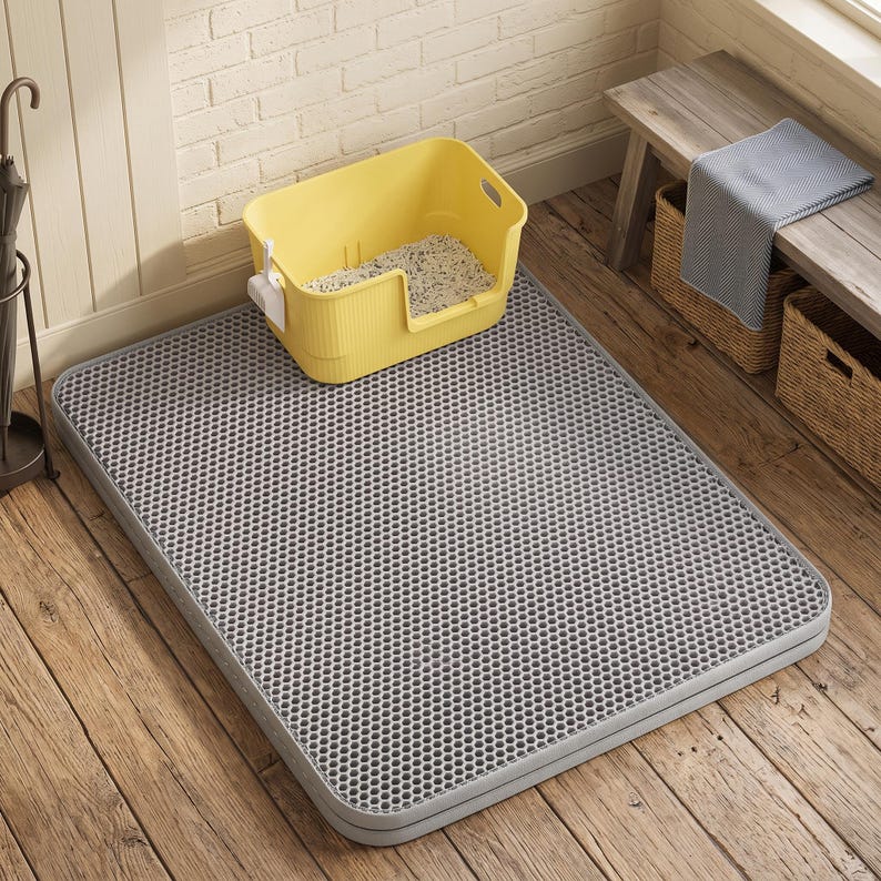 May include: A rectangular grey cat litter mat with a honeycomb-patterned top surface. A bright yellow plastic cat litter box containing white litter and a small white scoop is positioned on the mat. The mat has a dual-layer design.