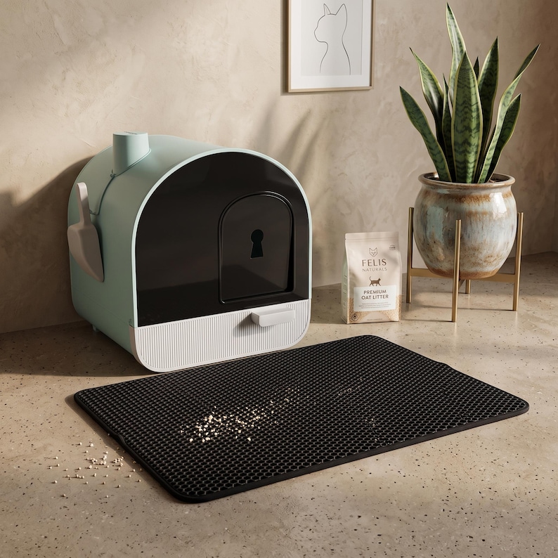 May include: A sage green and black enclosed cat litter box with a keyhole-shaped door, a matching scoop, a bag of Felis Naturals Premium Oat Litter, and a black rectangular honeycomb-patterned litter mat with scattered litter particles.