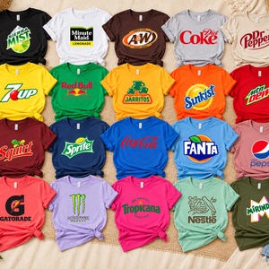 May include: A collection of twenty short-sleeved t-shirts in various solid colours, each featuring a different beverage brand logo printed on the front, including Sierra Mist, Minute Maid, A&W, Diet Coke, Dr Pepper, 7Up, Red Bull, Jarritos, Sunkist, Mtn Dew, Squirt, Sprite, Coca-Cola, Fanta, Pepsi, Gatorade, Monster, Tropicana, Nestlé, and Mirinda.