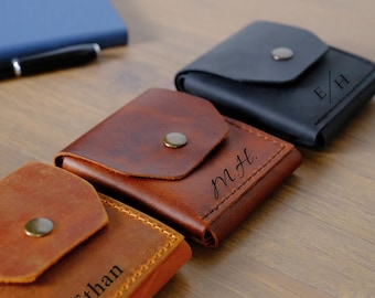 May include: Three square leather pouches with snap closures. One is black with the engraved letters E/H, one is medium brown with the engraved letters M.H., and one is light brown with the engraved name Ethan. Each pouch features visible stitching.