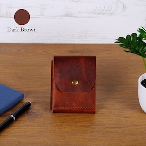 May include: A dark brown leather wallet featuring a rectangular flap closure secured with a single brass-toned metal snap button. The wallet has visible stitching along the bottom edge and a smooth, matte texture throughout its surface.