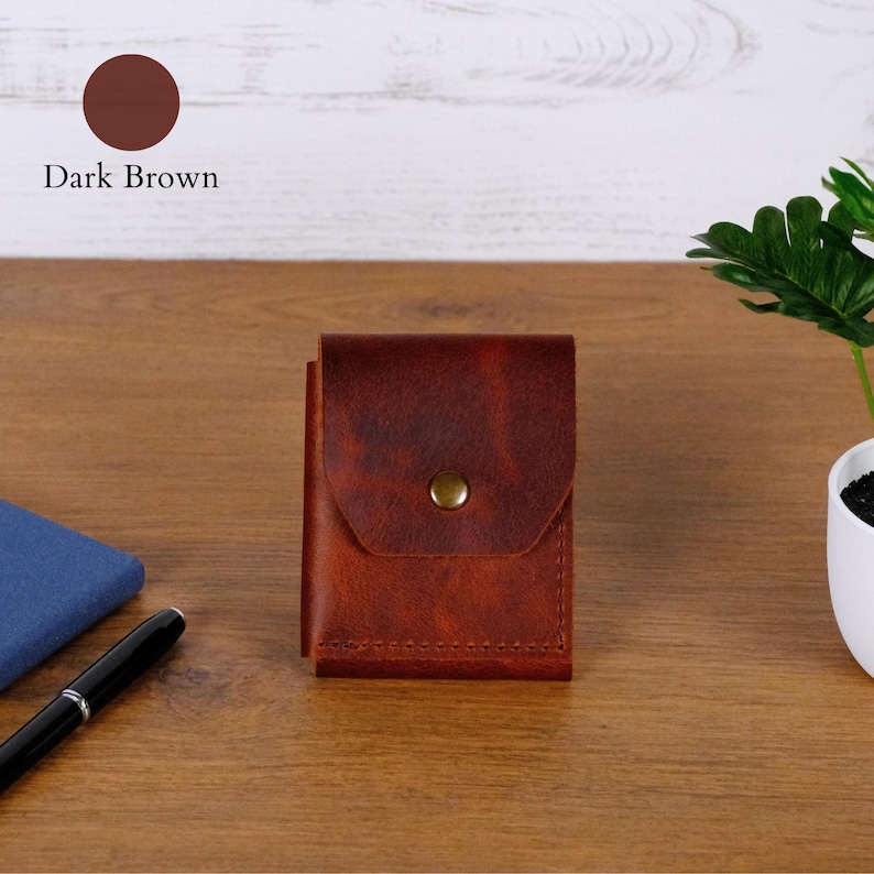 May include: A dark brown leather wallet featuring a rectangular flap closure secured with a single brass-toned metal snap button. The wallet has visible stitching along the bottom edge and a smooth, matte texture throughout its surface.