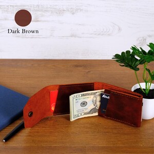 May include: A dark brown leather bifold wallet featuring a snap button closure, internal slots holding a red credit card, a black credit card, and a twenty-dollar bill. A black pen is tucked into the side of the open wallet structure.