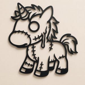 May include: A black wall art piece shaped like a stylized unicorn with a single horn, a circular eye, and stitched details across the muzzle, neck, and legs. The design features a flowing mane and tail with a dripping effect near the eye area.