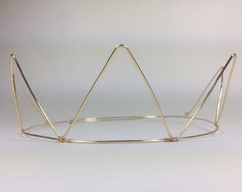 May include: A gold-colored wire crown with a circular base and triangular peaks. The crown is made of thin, bent wire, and the design is simple and elegant. The crown is likely for a costume or decorative purpose.