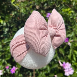 May include: A pink fabric headband with a large, knotted bow. The headband is made of a soft, stretchy material and is perfect for adding a touch of style to any outfit.