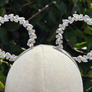 May include: A pair of silver rhinestone headband ears. The headband is made of a thin silver wire and is decorated with clear rhinestones arranged in a leaf pattern.