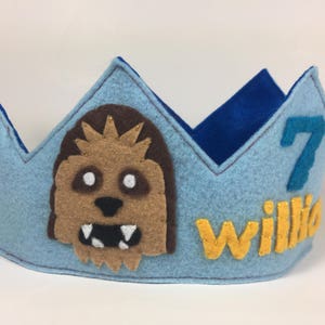 May include: Blue felt crown with a brown felt Chewbacca character, a yellow felt "Willa" name, and a blue felt number 7.