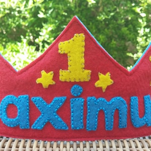May include: Red felt crown with a blue felt name "maximus" and a yellow felt number "1" in the center. The crown is decorated with yellow felt stars.