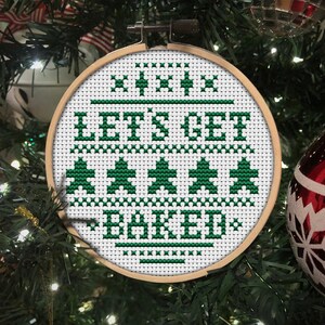 May include: A white embroidery hoop with green thread, depicting a Christmas-themed design that reads "Let's Get Baked".