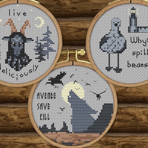 May include: Three embroidery hoops with different designs. The first hoop has a black goat with horns and the text "live deliciously". The second hoop has a black and white bird with the text "Why'd ye spill yer beans?". The third hoop has a black wolf with the text "avenge save kill".