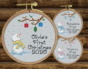 May include: Three circular wooden embroidery hoops containing cross-stitch designs of snowmen with colorful scarves and hanging ornaments. The text reads Olivia's First Christmas 2026, Benjamin's First Christmas 2026, and Violet's First Christmas 2026.