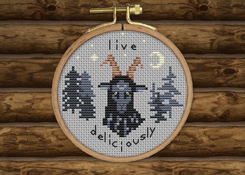 May include: Embroidered hoop art featuring a black goat with horns and a crescent moon in the background. The text "live deliciously" is stitched below the goat.