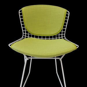 May include: A mid-century modern chair with a white wire frame and a lime green seat and backrest. The chair has a curved seat and back, and the legs are angled for stability. The chair is a stylish piece of furniture.