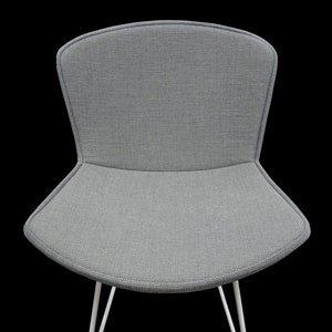 Op de afbeelding: Een grijze stoel van stof met een wit metalen frame. De stoel heeft een gebogen rugleuning en een brede zitting.