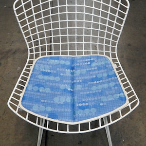 May include: White wire chair with a blue and white patterned cushion. The chair has a curved back and a simple design.