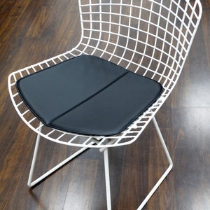 May include: White wire chair with a black cushion. The chair has a simple, modern design and is made of metal.