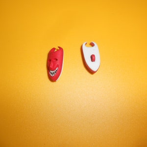 May include: Two small plastic masks, one red with a white face and a toothy grin, the other white with a red face and a small red circle.