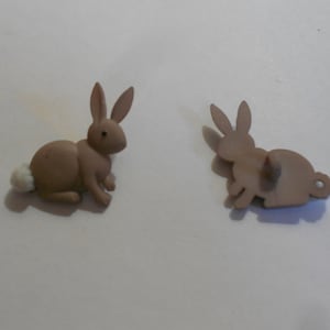 May include: Two brown ceramic bunny buttons with white accents. One button shows the front of the bunny and the other shows the back.