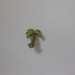 Op de afbeelding: Een klein, groen palmboomfiguurtje met een bruine stam. Het figuurtje is gemaakt van hout en heeft een eenvoudig, cartoonachtig ontwerp.