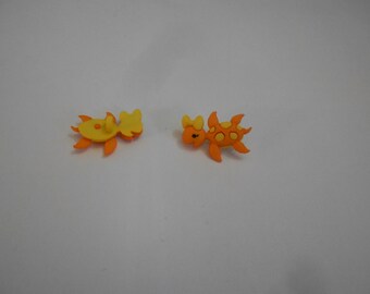 May include: Two colourful plastic buttons shaped like a turtle and a crab. The turtle is orange with yellow spots and the crab is yellow with orange legs.
