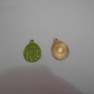 May include: Two oval-shaped pendants. One is green with a gold filigree design and a gold border. The other pendant is gold with a sunburst pattern on the back. Both have a small loop at the top for hanging.