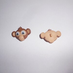 May include: A brown plastic monkey button with googly eyes. The back of the button is plain brown.